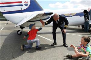 A white pilot high fives a little boy under the wing of a small plane